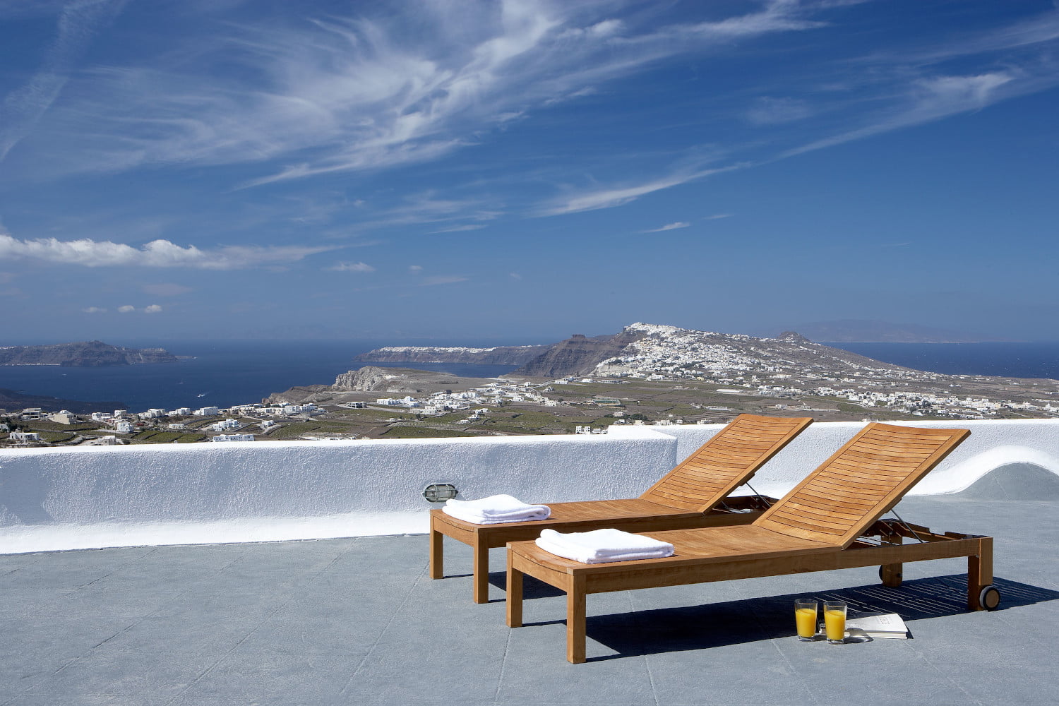 Grey terrace, white wall, blue sky, island view, 2 sunbeds, orange juices and towels at the Pyrgos Santorini Casa Vinios by Rent A Greek Home Path Travel Designs