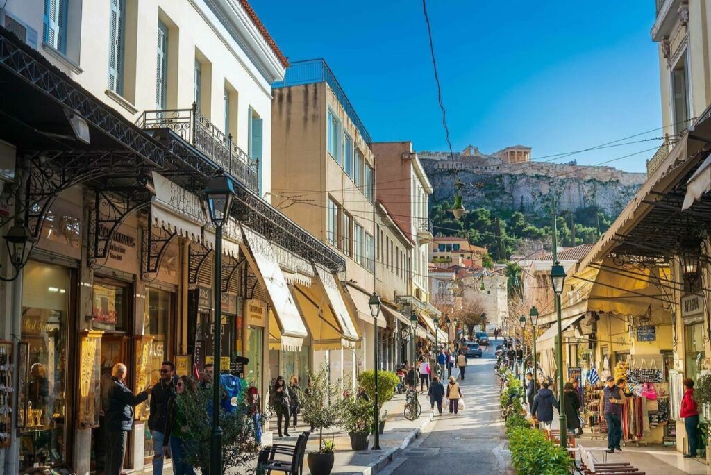 Athens Acropolis | Visiting Athens in the winter Locals and travellers who are visiting Athens in the winter dressed in sweaters and jackets enjoying the winter sun while strooling through the streets beneath the Acropolis on a clear day with a blue sky