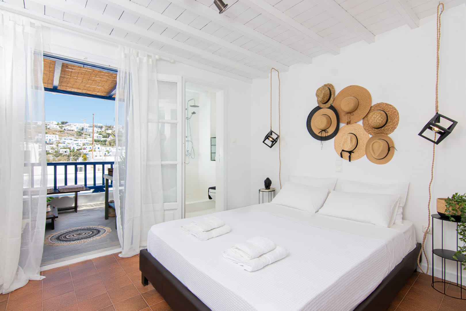 The boho decorated bedroom of the Mykonos Town loft Casa Rosalia by Rent A Greek Home includes a selections of hats right over the bed